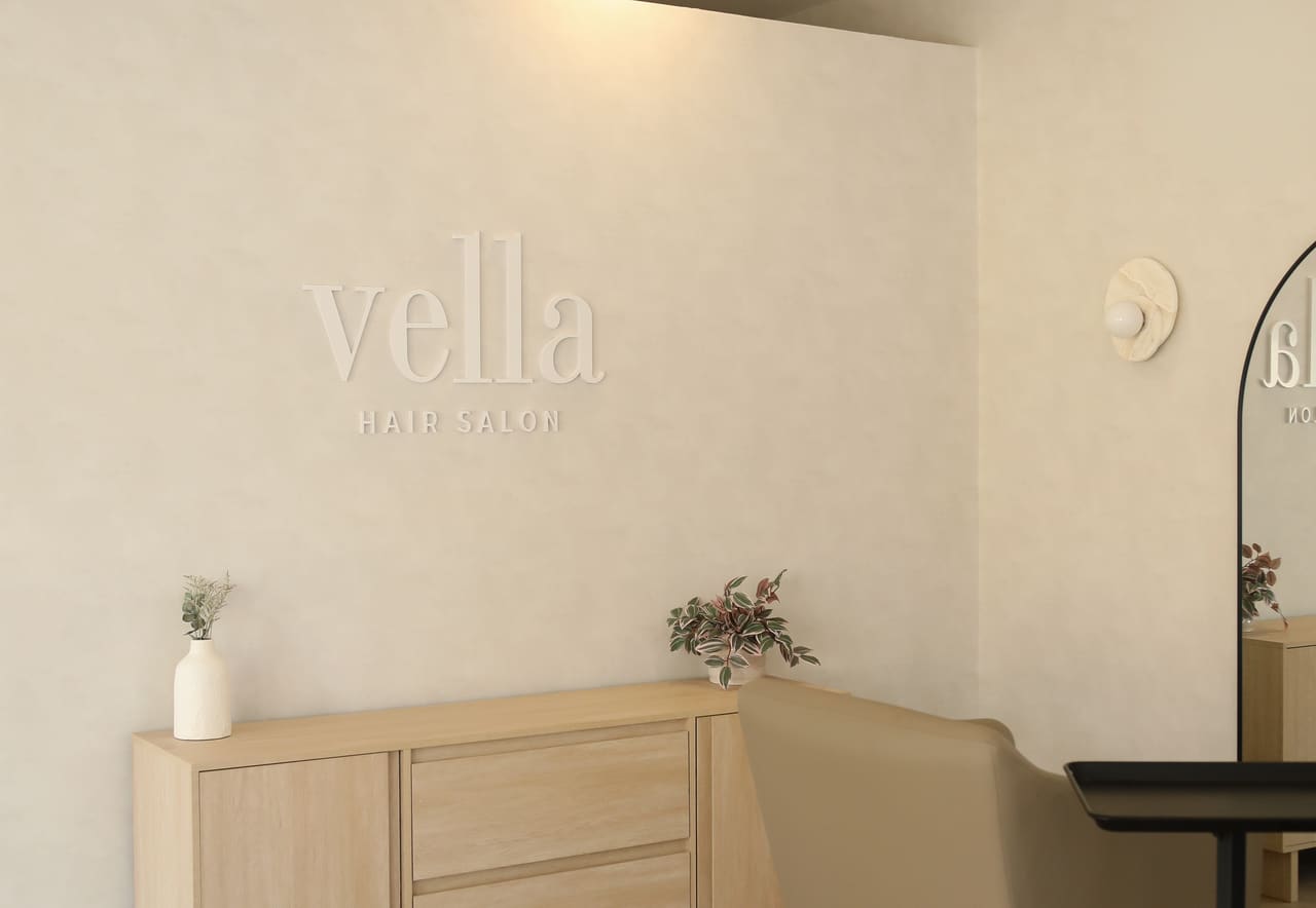 Inside Vella Hair Salon — the vella hair salon wall sign above a styling chair and light oak cabinetry